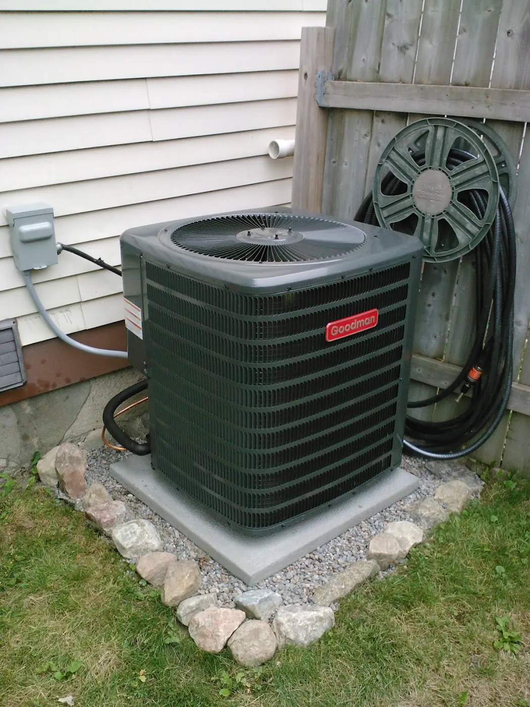 Outdoor Goodman air conditioner installed on a gravel pad beside a home